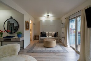 Un salon moderne avec un canapé, une table basse, un tapis rond, un miroir et un téléviseur fixé sur une porte coulissante.