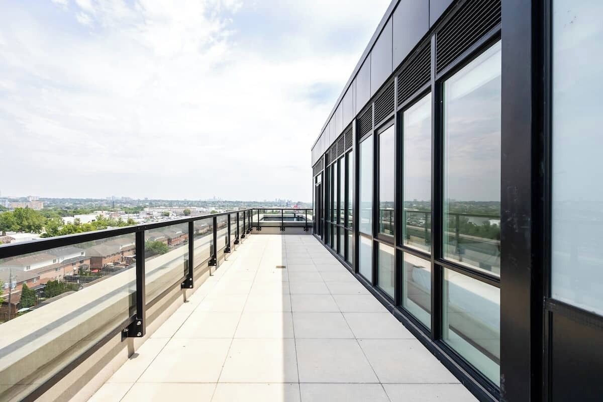 Ein langer, schmaler Balkon mit Metallgeländer, großen Fenstern und Blick auf die Stadt.