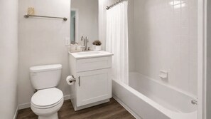 A bathroom with a toilet, sink, cabinet, and bathtub.