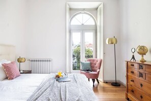 Un dormitorio con cama, cómoda, silla, radiador y ventana con vistas.