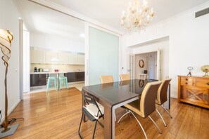 Un comedor moderno con una mesa y sillas de vidrio, una araña y un aparador de madera con cajones.