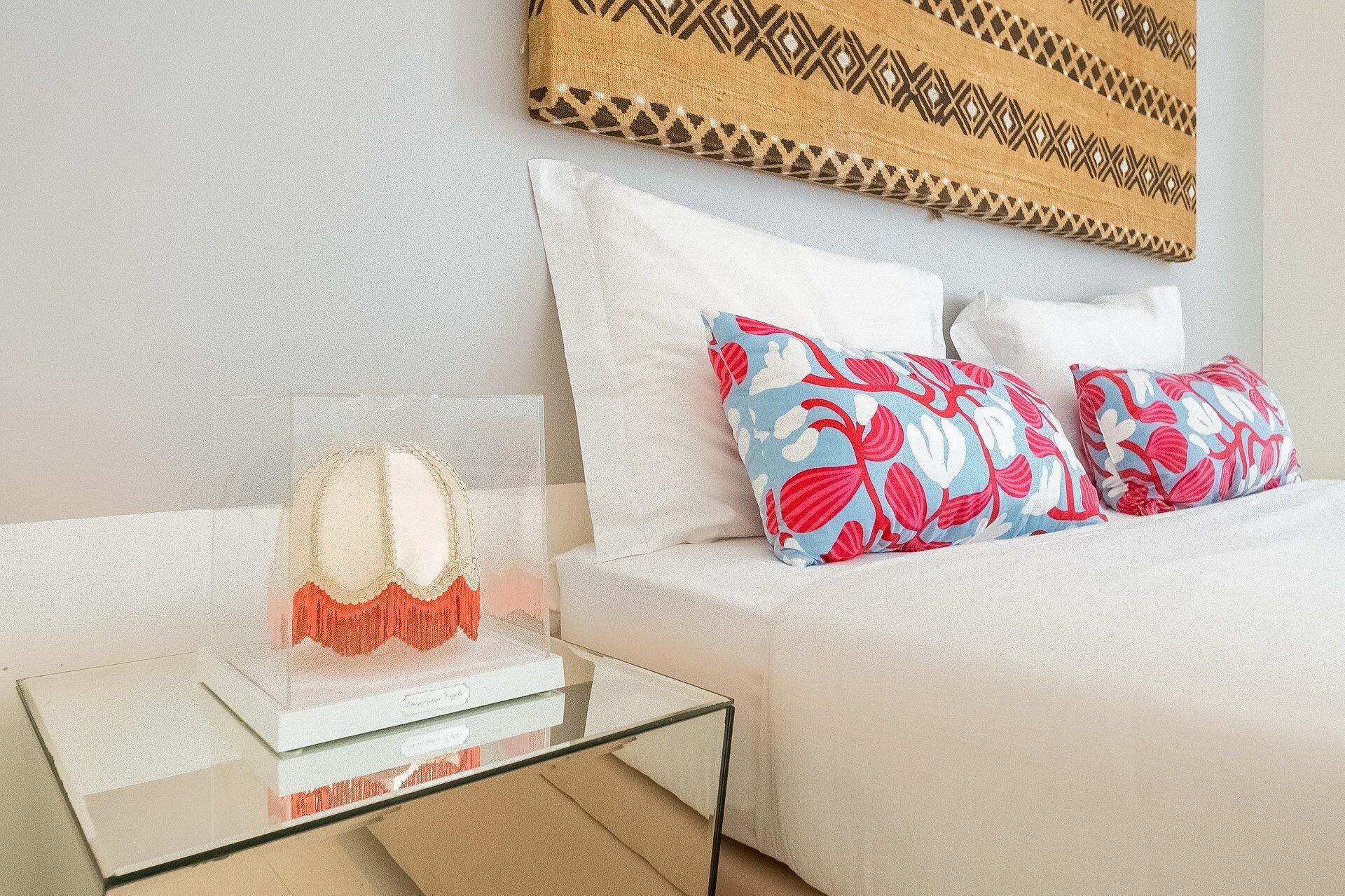 A neatly made bed with white bedding and two decorative pillows with a red and blue floral pattern.