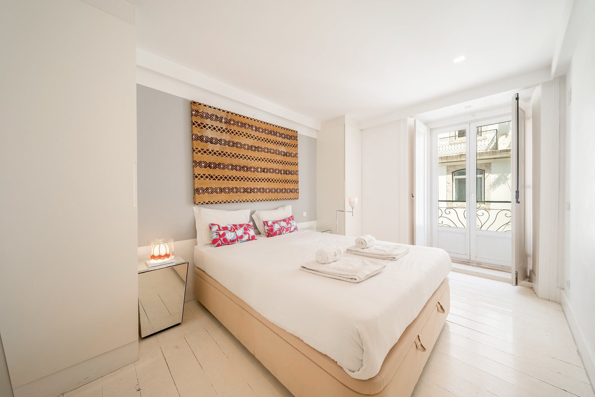 Ein Hotelzimmer mit Bett, Nachttisch, Lampe und Blick ins Freie.