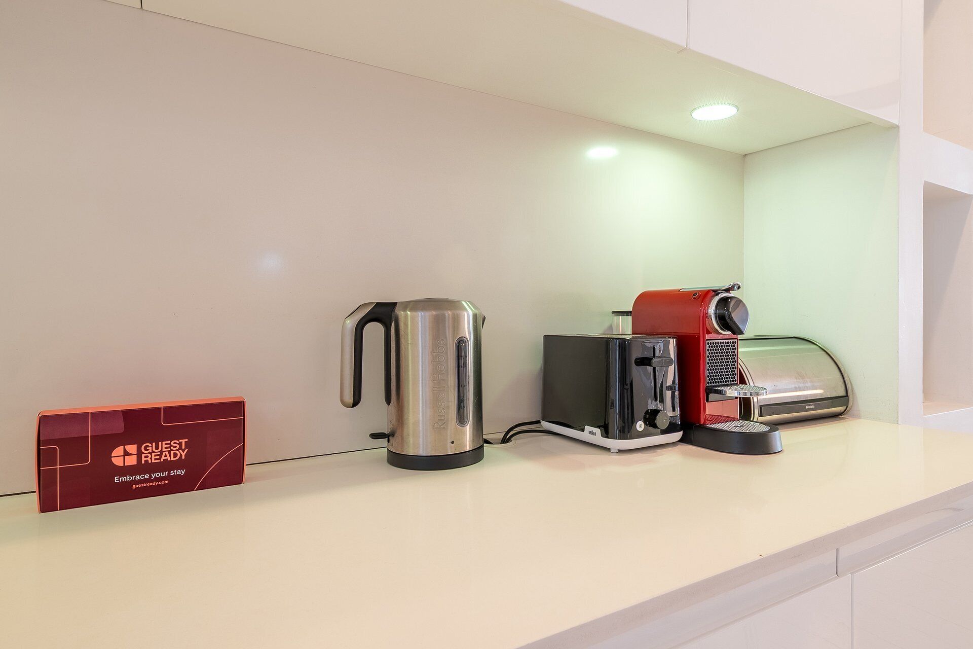 Une petite cuisine équipée d’une machine à café, d’un grille-pain et d’une boîte rouge portant l’inscription « PRÊT POUR LES CLIENTS ».