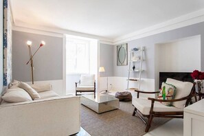 A living room with a sofa, armchairs, a coffee table, and a lamp. There is a window providing natural light and a fireplace. - GuestReady - Wonderful flat near the Pink Street (Lisbon)