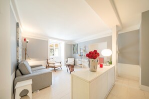 Ein modernes Wohnzimmer mit einer Couch, Sesseln, einem Couchtisch, einem weißen Konsolentisch mit Blumen und einer Stehlampe.