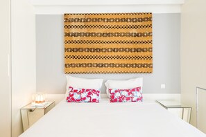 Ein Hotelzimmer mit einem Bett, zwei Kissen mit Blumenmuster, einem Nachttisch mit Lampe und einem Wandteppich.