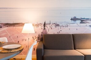 Ein Zimmer mit Blick auf einen Hafen, eine Couch, ein Tisch mit Teller und Besteck sowie eine Lampe.