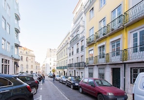 Eine Straße gesäumt von mehrstöckigen Gebäuden, parkenden Autos und Fußgängern.