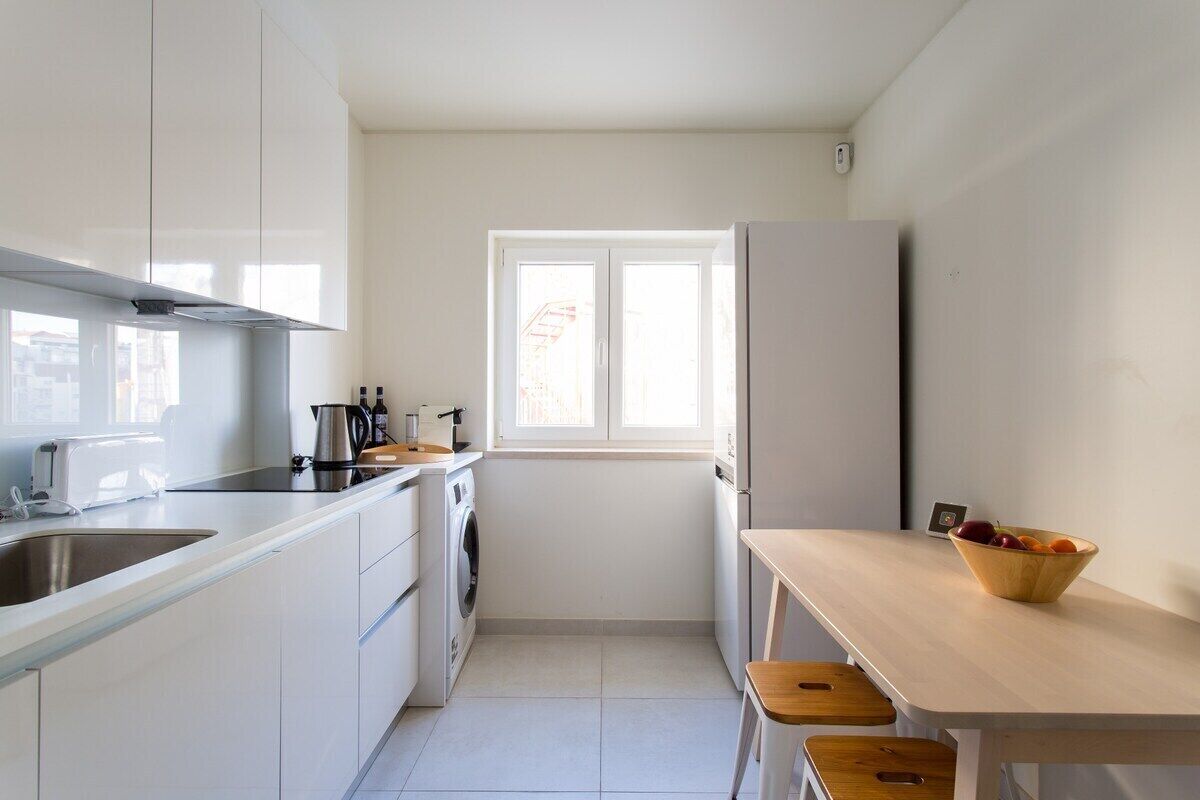 A compact kitchen with white cabinets, a built-in oven, a sink, and a window providing natural light.