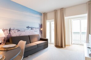A modern hotel room with a sofa, a dining table, and a view of a cityscape through a large window. - GuestReady - Stylish stay near the National Museum (Lisbon)