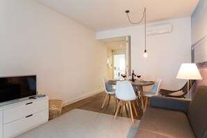 Ein modernes Wohnzimmer mit Flachbildfernseher, Esstisch mit Stühlen, Sofa und Lampe.