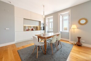 A modern kitchen with white cabinetry, a wooden dining table, and a gray rug. - GuestReady - Fantastic flat near S. Jorge Castle (Lisbon)