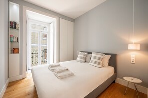 Una camera da letto con un letto, cuscini, un comodino, una lampada e vista su un balcone.