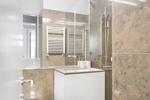 Un bagno moderno con box doccia in vetro, lavandino bianco e porta asciugamani.