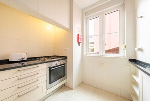 Une cuisine équipée d’une cuisinière à gaz, d’un four et d’une fenêtre donnant sur les bâtiments environnants.