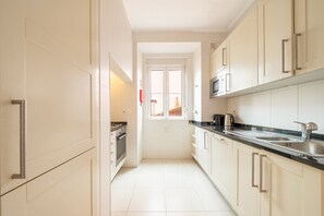 A narrow kitchen with white cabinets, a stainless steel sink, and a microwave. - GuestReady - Stunning flat in Principe Real (Lisbon)