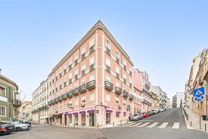 A pink building with multiple floors, balconies, and a pedestrian crossing. - GuestReady - Stunning flat in Principe Real (Lisbon)
