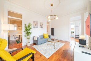 A modern living room with a sofa, a coffee table, and a yellow armchair. There is a potted plant and artwork on the walls. - GuestReady - Stunning flat in Principe Real (Lisbon)