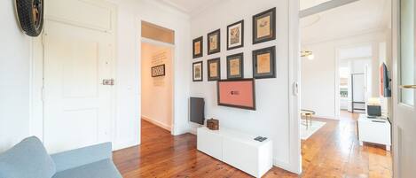 A spacious living area with a wooden floor, a white bench, and a wall adorned with framed certificates.