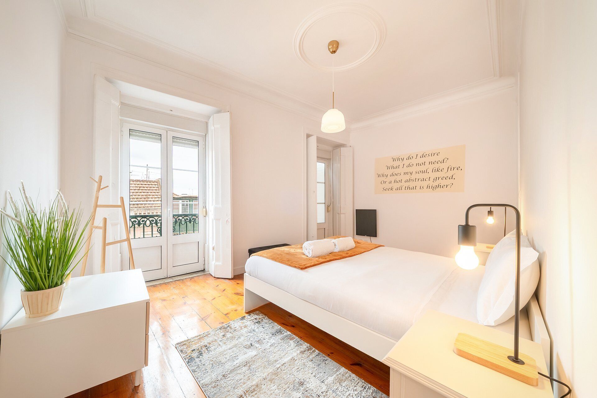 A bedroom with a bed, bedside table, lamp, and a wall with a quote.