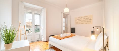 A bedroom with a bed, bedside table, lamp, and a wall with a quote.