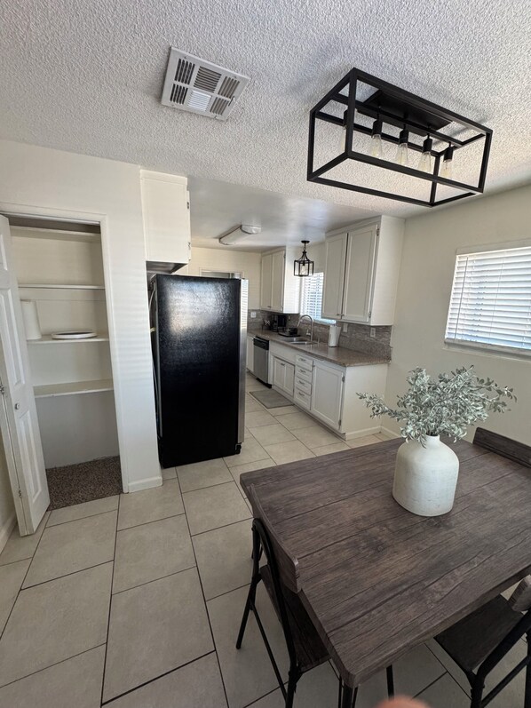A kitchen with a black refrigerator, white cabinets, a dining table with chairs, and a potted plant.