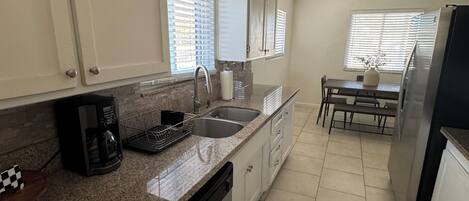A kitchen with a dishwasher, a coffee maker, and a dining area with a table and chairs.