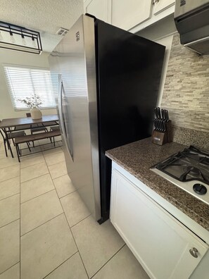 A modern kitchen with a stainless steel refrigerator, granite countertop, and a gas stove.