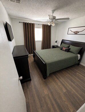 A bedroom with a bed, a nightstand, a ceiling fan, and a window with curtains.