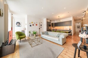 A modern living room with a sofa, chairs, a coffee table, and a kitchen in the background. - GuestReady - Gorgeous stay near Time Out Market (Lisbon)