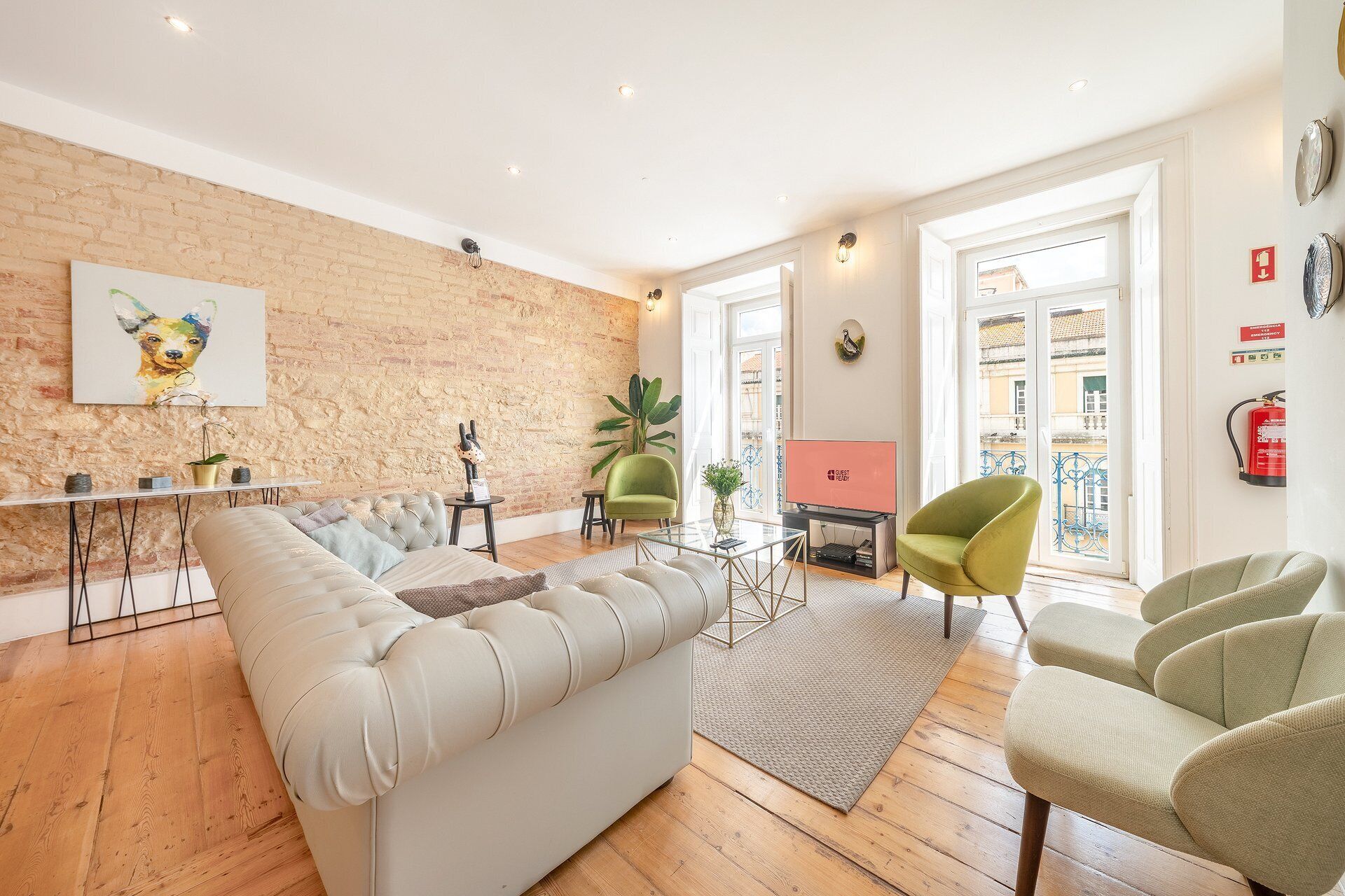A living room with a brick wall, a sofa, a television, and a green armchair.