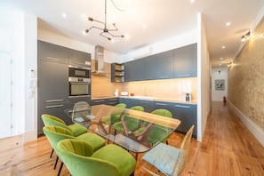 A modern kitchen with grey cabinets, a glass dining table, and green chairs. - GuestReady - Gorgeous stay near Time Out Market (Lisbon)
