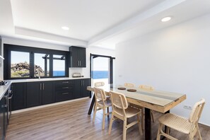 A modern kitchen with dark cabinets, a wooden dining table, and wicker chairs. - TenoHomes Lava and Atlantic Views Garachico (Garachico)