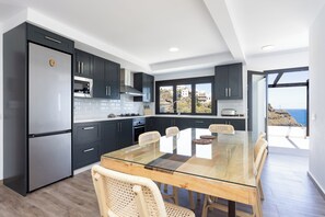 A modern kitchen with dark cabinetry, a glass-top dining table, and a view of the sea. - TenoHomes Lava and Atlantic Views Garachico (Garachico)