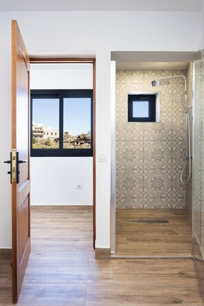 Ein Zimmer mit Holzboden, einem Fenster mit Blick auf Gebäude und einem Duschbereich mit gemusterten Fliesen.