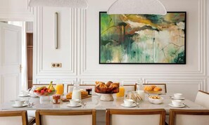 Un comedor con una mesa dispuesta para el desayuno, que incluye frutas, pasteles y bebidas.