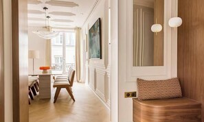 Habitación de hotel con un banco de madera, una zona de comedor con mesa y sillas, un cuadro en la pared y una lámpara de araña.