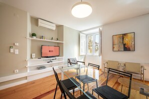 A modern living room with a TV, shelves, and a dining area with chairs and a table. - GuestReady - Chic flat near Lisbon Cathedral (Lisbon)