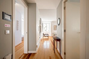 A hallway with wooden flooring, a door on the right, and a window at the end. - GuestReady - Chic flat near Lisbon Cathedral (Lisbon)