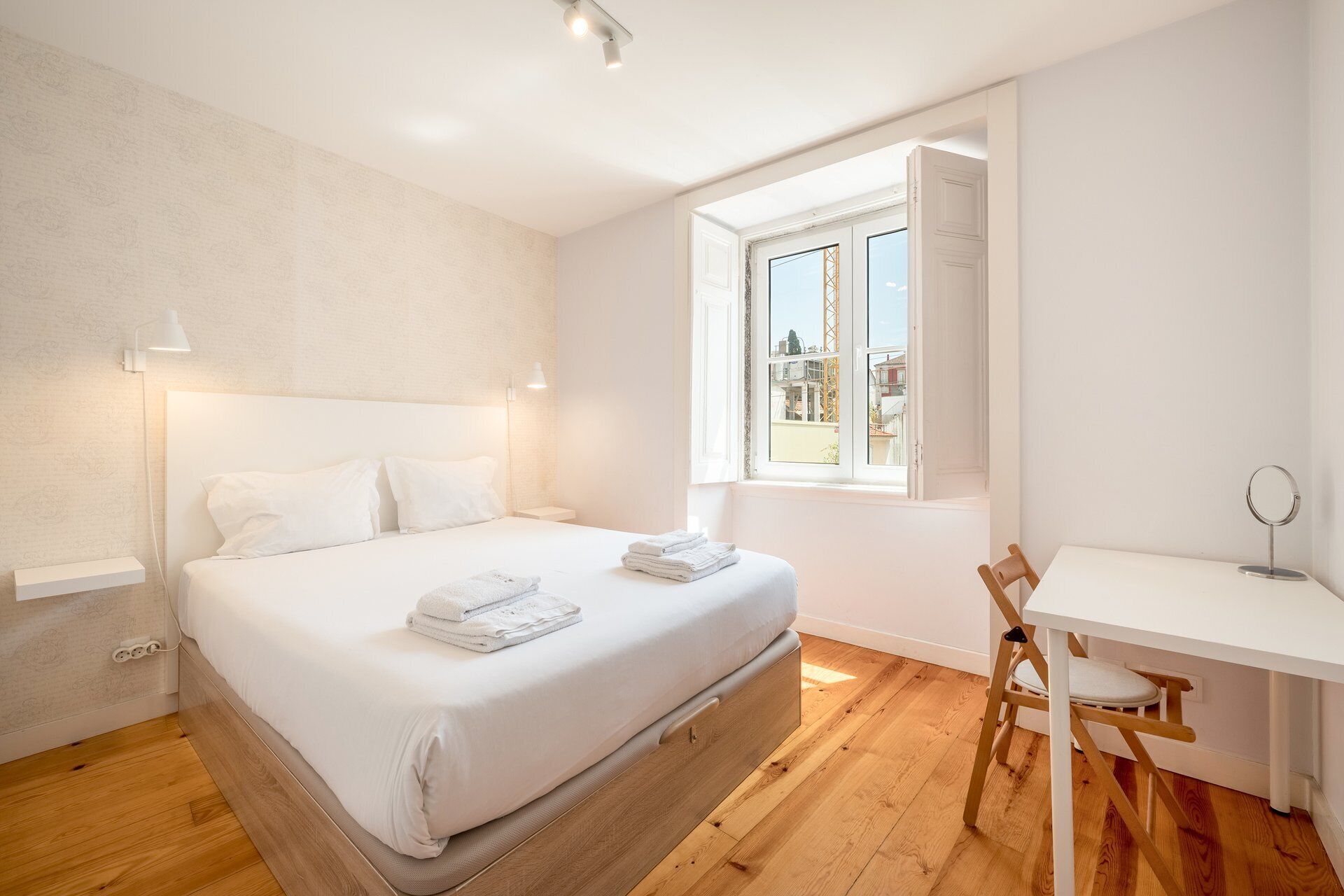 A bedroom with a bed, bedside lamps, a desk with a chair, and a window with a view.