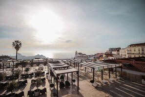 Eine Terrasse im Freien mit Tischen und Stühlen mit Blick auf eine Stadtlandschaft und das Meer.