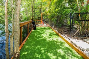 A pathway with artificial grass, surrounded by trees and a wooden railing. - Tropical 5BR Retreat ! Pool, Bar, Games & Nature (Sunrise)