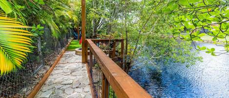 A wooden pathway leading to a water body, surrounded by lush greenery and a chain-link fence.