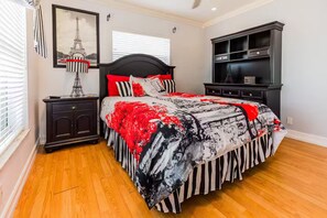 A bedroom with a bed, nightstand, dresser, and a wall-mounted lamp. - Tropical 5BR Retreat ! Pool, Bar, Games & Nature (Sunrise)