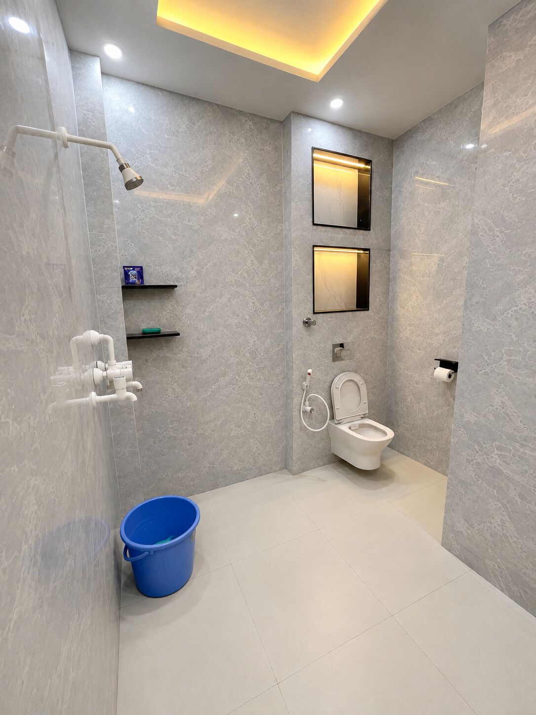 Et moderne badeværelse med bruser, toilet og en blå spand.