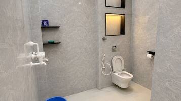 Et moderne badeværelse med bruser, toilet og en blå spand.