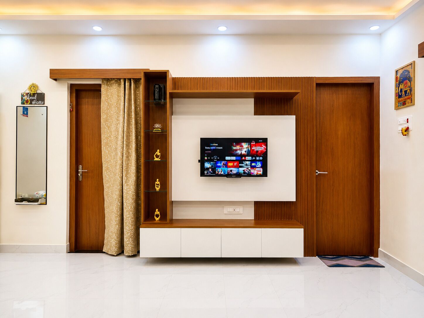 A modern living room with a flat-screen TV mounted on a wooden wall unit, a door with a mirror, and a decorative sign.
