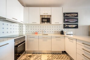 Een moderne keuken met witte kastjes, een roestvrijstalen oven, een magnetron en een spoelbak. Op de muur hangen twee vis-schilderijen.