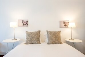 Een hotelkamer met een bed, twee nachtkastjes, twee lampen en twee kunstwerken aan de muur.